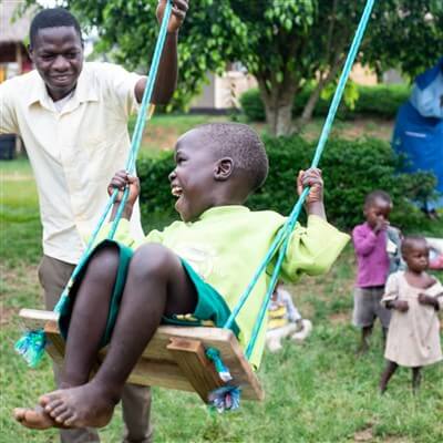 Staff member plays with an orphaned child on a swing in Uganda.